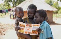 ثلاثة أطفال في السودان يقرؤون كتيبا 