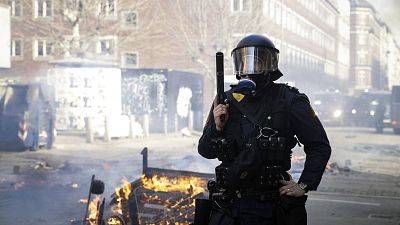 Agentes de policía daneses hacen guardia junto a un fuego encendido por personas que protestaban en un barrio de inmigrantes en Copenhague, el domingo 14 de abril de 2019.