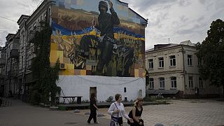 Des gens passent devant une œuvre d'art sur le côté d'un immeuble résidentiel, à Kiev, en Ukraine, le samedi 26 août 2023.