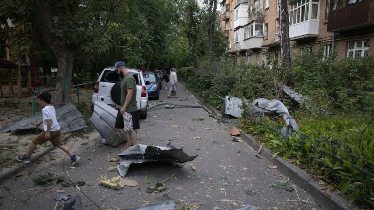 Des habitants passent devant les débris tombés de leur maison endommagée après une attaque à la roquette russe à Kyiv, le 30 août
