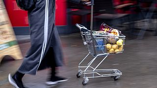 Μια γυναίκα σπρώχνει ένα μικρό καροτσάκι αγορών έξω από discount σουπερ μαρκετ