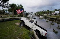 A pickup truck with an American flag tied to sits halfway into a canal in Horseshoe Beach, Fla., after the passage of Hurricane Idalia, Wednesday, Aug. 30, 2023.