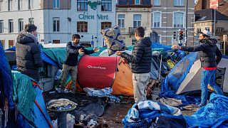 Brüksel'deki Petit Chateau kabul merkezinin dışında kurulan derme çatma çadır kampında erkekler eşyalarını düzenliyor