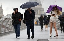  People shield themselves from the rain while crossing Millennium Bridge in London.