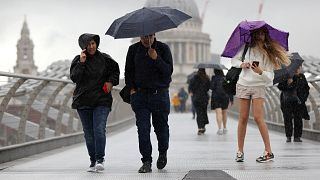  People shield themselves from the rain while crossing Millennium Bridge in London.