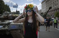 Une femme porte une guirlande de fleurs devant des chars russes capturés, exposés sur la place centrale Khreshchatyk à Kiev, en Ukraine. 24 août 2023