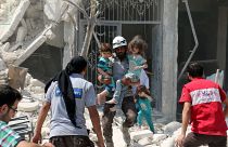أطفال يقفون بجانب منزلهم المتضرر في قرية باريشا في محافظة إدلب