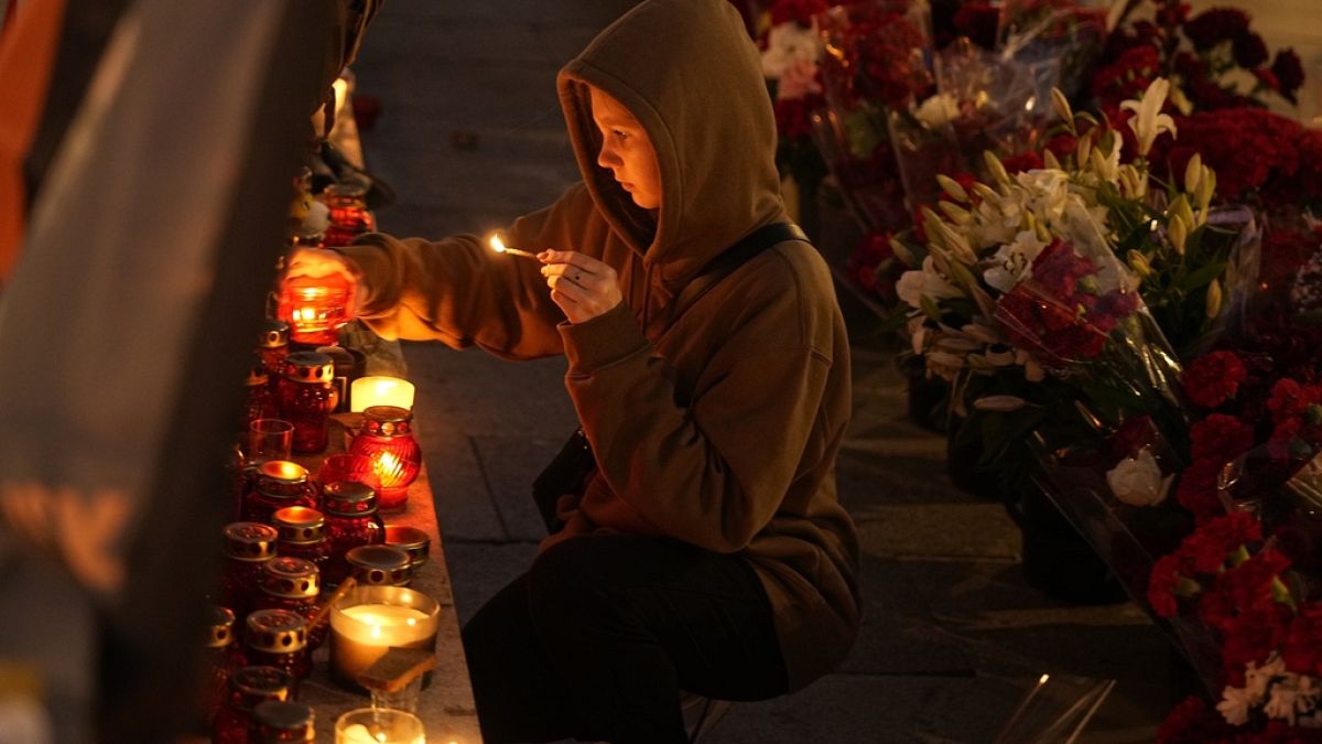 A young woman lights a candle at an informal street memorial with flowers and lit candles for Wagner Group's military group members killed in a plane crash