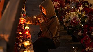 A young woman lights a candle at an informal street memorial with flowers and lit candles for Wagner Group's military group members killed in a plane crash