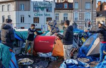 ARQUIVO - Homens organizam os seus pertences num acampamento improvisado em frente ao centro de acolhimento Petit Chateau, em Bruxelas, a 17 de janeiro de 2023.
