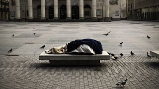 Бездомный человек спит на лавке в центре европейского города
