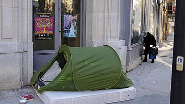 Uma mulher está numa rua ao lado de uma tenda para sem-abrigo, em Paris, França, terça-feira, 21 de dezembro de 2021. 