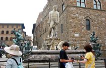 File -Tourists look on by the statue of the Neptune by Italian 16th century artist Bartolomeo Ammannati in Florence's Piazza della Signoria square, 2005