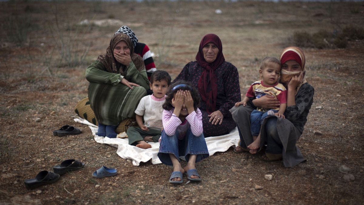 Сирийская семья, бежавшая от насилия в своей деревне, сидит на земле в лагере для перемещенных лиц недалеко от границы с Турцией.