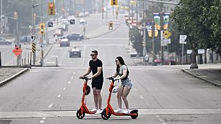 People cross Elgin Street on rental e-scooters as haze from wildfire smoke is seen in the air, in Ottawa.