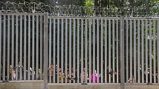 FILE - Migrants seeking asylum look through a fence that Poland has built on its border with Belarus, in Bialowieza, Poland, on Sunday, 28 May 2023.