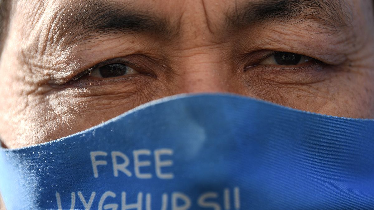 أحد أفراد أقلية الإيغور يرتدي قناع وجه يعرض علم تركستان الشرقية أثناء تظاهرهم 