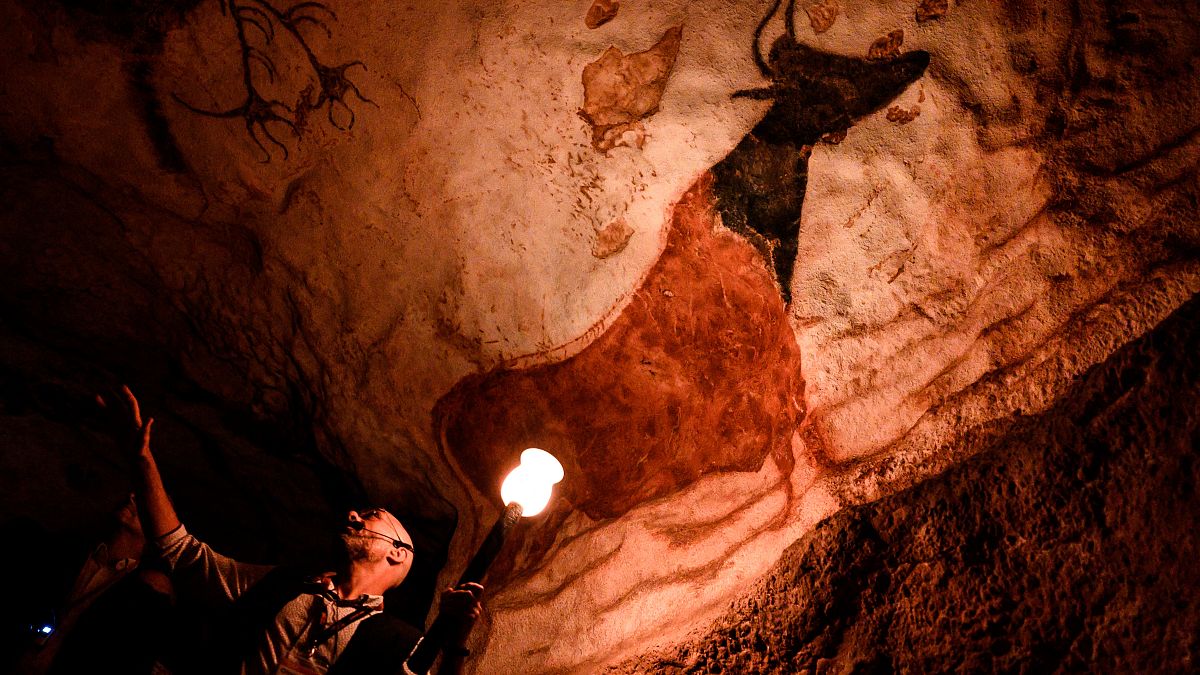 An employee shows paintings inside the life size Lascaux cave replica during a special immersive torch light visit, 2022