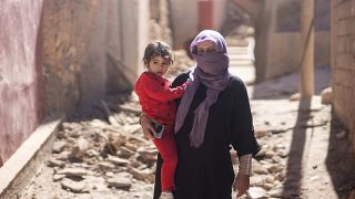 سيدة وابنتها تقفان خارج منزلهما المدمر إثر الزلزال الذي ضرب قرية مولاي إبراهيم، مراكش، المغرب.