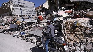 Homem conduz ladeado de escombros onde resiste um sinal com indicação de Marraquexe, Marrocos