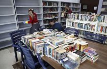 أشخاص ينظفون رفوف كتب في مكتبة مدرسة في اللويزة قرب بيروت