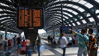 Viaggiatori controllano sui tabelloni ferroviari le variazioni degli orari alla stazione centrale di Milano