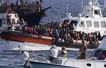 An Italian Coast Guard boat carries migrants as tourists on boat, foreground, watch, near the port of the Sicilian island of Lampedusa, southern Italy, Monday, Sept. 18, 2023.