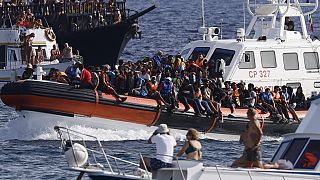 An Italian Coast Guard boat carries migrants as tourists on boat, foreground, watch, near the port of the Sicilian island of Lampedusa, southern Italy, Monday, Sept. 18, 2023.