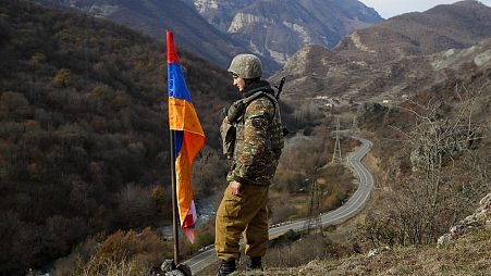 FILE - In this Wednesday, Nov. 25, 2020 file photo, an ethnic Armenian soldier stands guard next to Nagorno-Karabakh's flag atop of the hill.