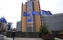 Flags flap in the wind as a man with flowers walks by EU headquarters in Brussels, Wednesday, Sept. 20, 2023.