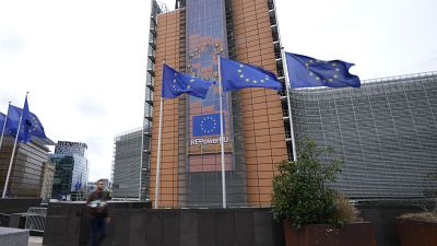 Flags flap in the wind as a man with flowers walks by EU headquarters in Brussels, Wednesday, Sept. 20, 2023.