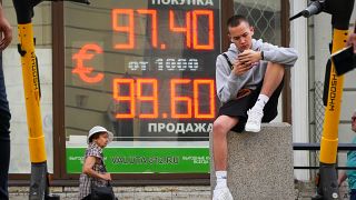 شاب يجلس بجوار شاشة تعرض أسعار صرف العملات من الدولار الأمريكي إلى الروبل الروسي في سانت بطرسبرغ - روسيا. 2023/07/06