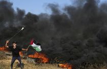 متظاهر فلسطيني يستخدم المقلاع لإلقاء الحجارة بينما يلوح بالعلم الفلسطيني بينما يحرق آخرون الإطارات خلال صدامات مع القوات الإسرائيلية شمال قطاع غزة. 2023/09/22