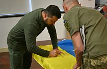 Il presidente ucraino Volodymir Zelensky autografa la bandiera nazionale per un soldato