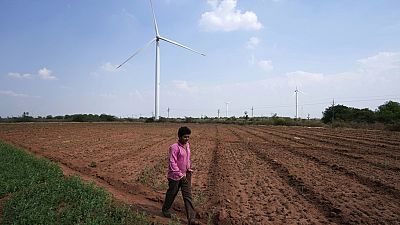 File - A boy walks on a field near wind turbines near Sadla village in Surendranagar district of Gujarat state, India, March 20, 2023.
