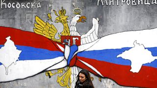 FILE - A woman walks by graffiti showing the Serbian flag, left, and Russian flags with maps of Kosovo and Crimea in northern Kosovo, 15/12/2018. 