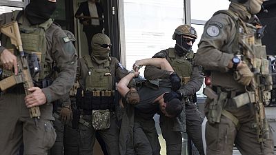 Miembros de la policía de Kosovo de la Unidad de Intervención Especial escoltan a uno de los pistoleros serbios arrestados fuera del tribunal después del tiroteo en Kosovo.