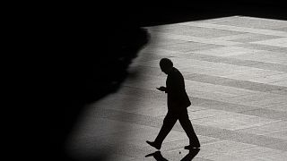 A man looks as his cell phone as he walks into the shadows in the business district in Madrid, Spain.