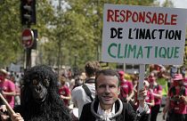 A protester wearing a mask depicting French President Emmanuel Macron holds a bord reading « Liable for climate inaction » during a rally in Paris, May 9, 2021.