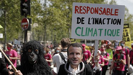 A protester wearing a mask depicting French President Emmanuel Macron holds a bord reading « Liable for climate inaction » during a rally in Paris, May 9, 2021.
