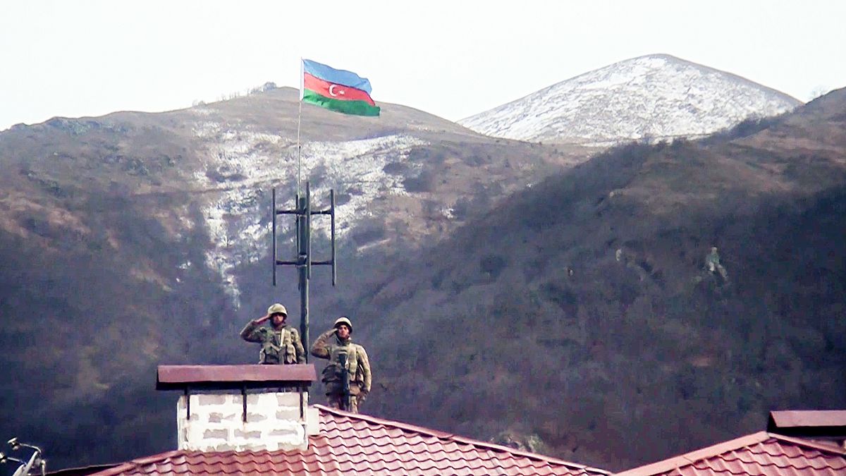 جنديان أذربيجانيان يؤديان التحية بينما يقفان على سطح ويحملان العلم الوطني الأذربيجاني عند دخولهما بلدة كالباجار المهجورة، أذربيجان