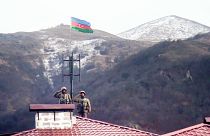 جنديان أذربيجانيان يؤديان التحية بينما يقفان على سطح ويحملان العلم الوطني الأذربيجاني عند دخولهما بلدة كالباجار المهجورة، أذربيجان