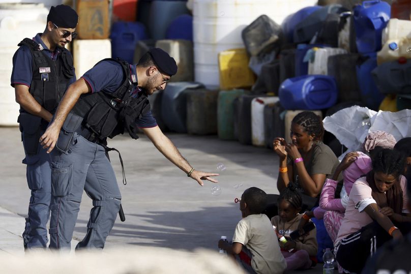 A police officer plays with a migrant child blowing soap bubbles in the port of the Sicilian island of Lampedusa, November 2023
