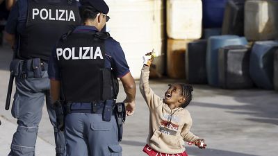 Agente da polícia olha para criança a brincar com bolas de sabão no porto de Lampedusa, Itália