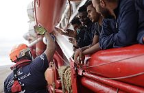Un voluntario de SOS Mediterranee choca los cinco con unos inmigrantes que se acercan a las costas italianas, el 4 de septiembre de 2022 frente a Taranto, en el sur de Italia.