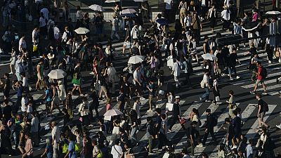 People carry umbrellas to shield themselves from the sun as they walk across an intersection Monday, July 17, 2023, in Tokyo. 