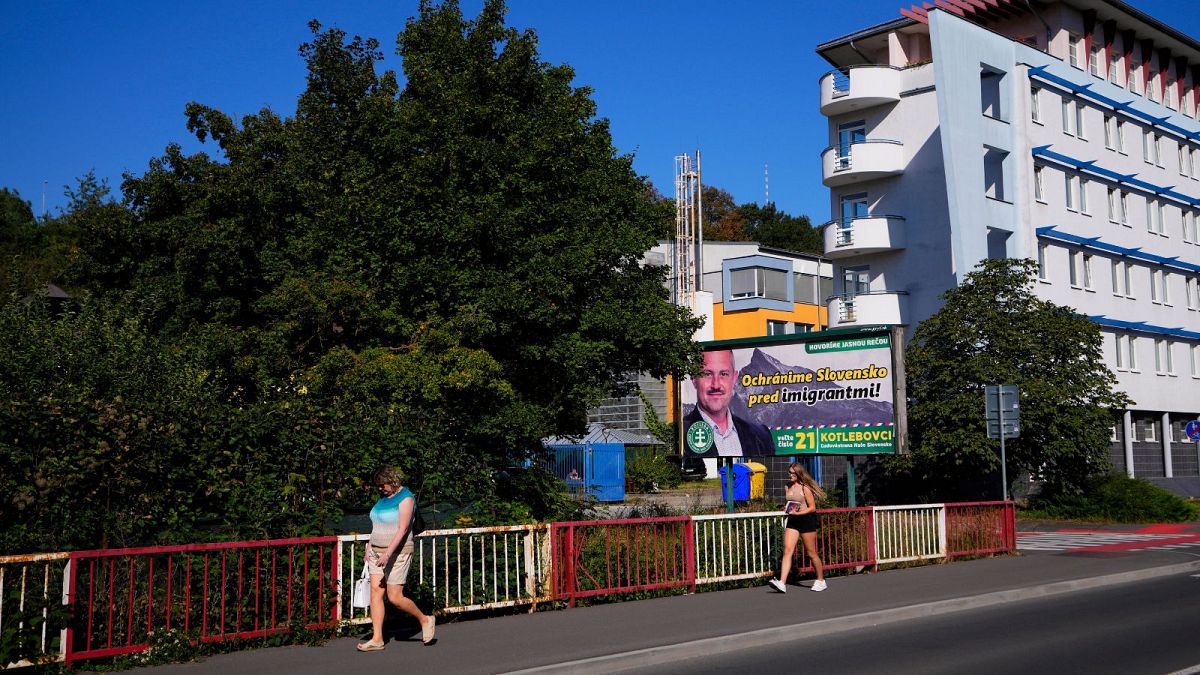 People pass an election billboard for the far-right Kotlebovci party in Banska Bystrica. The billboard reads: "We will save Slovakia from migrants".