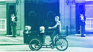 Ein Radfahrer fährt auf einem Lastenrad mit Kindern vor der Königlichen Leibgarde am Schloss Amalienborg in Kopenhagen, Juni 2023