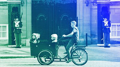 Un ciclista monta en una bicicleta de carga con niños delante de Los Guardias Reales de la Vida en el Castillo de Amalienborg en Copenhague, junio de 2023.