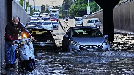 رجل يدفع دراجته النارية بينما تسير السيارات عبر طريق غمرته المياه بعد هطول أمطار غزيرة في الصباح الباكر، بيروت، لبنان، 4 أكتوبر، 2023.